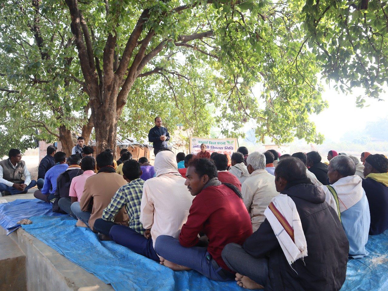 Villagers sitting together under a large tree for a meeting