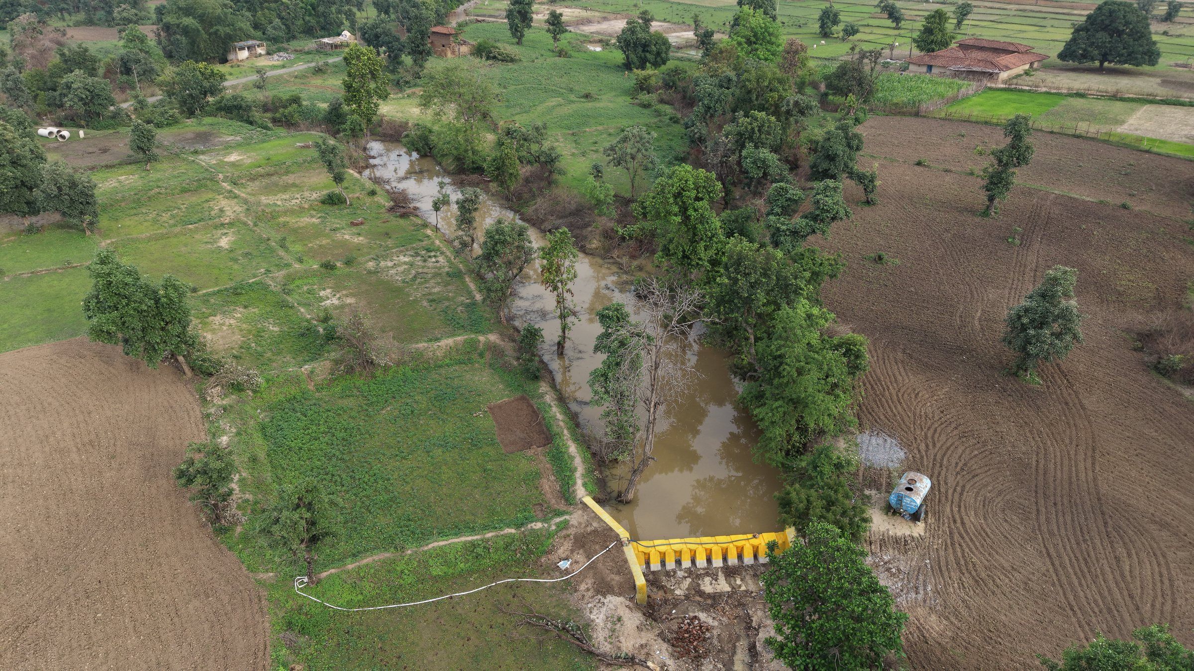 Aerial view of a drum check dam holding water in a green valley